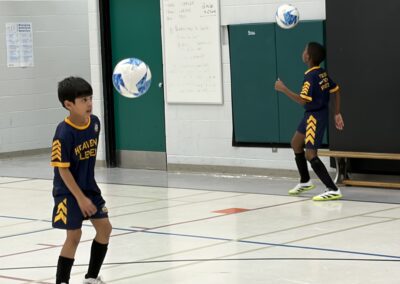 Two boys playing basketball indoors, one dribbling the ball.