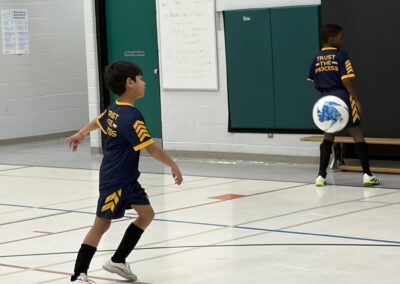 Child in sports uniform playing indoor soccer, kicking the ball.
