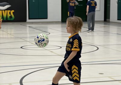 A young boy in soccer gear controlling a ball indoors.