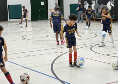 Young children playing soccer indoors in a gymnasium.