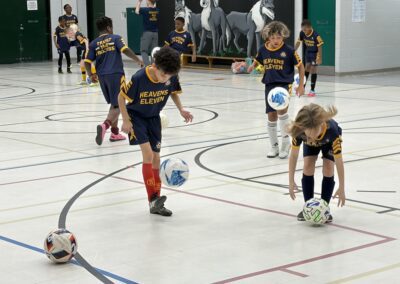 Young children playing indoor soccer, focusing on ball control.