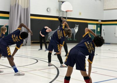 Youth basketball team stretching before practice in gym.