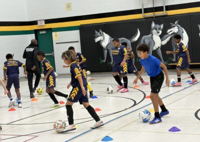Children practicing soccer drills indoors with cones and balls.