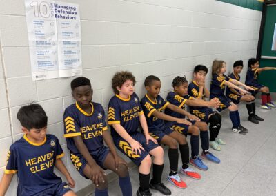 Youth soccer team sitting against wall.