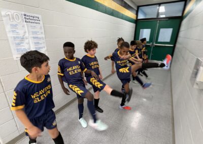 Young basketball players practicing leg stretches in a hallway.
