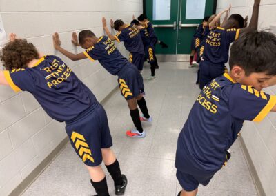 Kids stretching indoors wearing matching sports shirts.