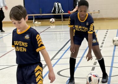Two boys in sports uniforms playing indoor soccer.