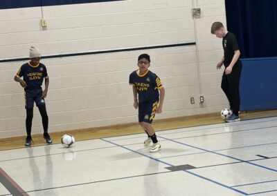 Youth soccer players practicing indoors with a coach.