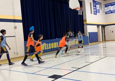Children playing basketball indoors in orange and white jerseys.