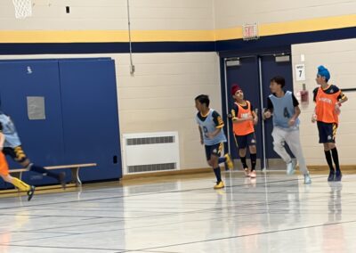 Three boys running indoors on a gym floor near a wall with doors.