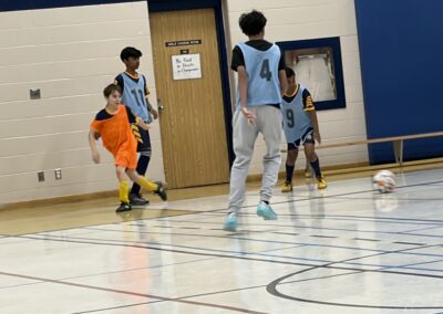 Young boys playing indoor soccer in a gym.