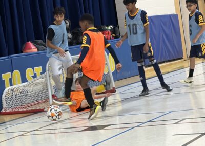 Young boys playing indoor soccer in a gymnasium.