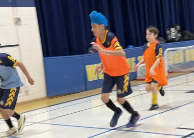Kids playing basketball indoors wearing orange jerseys.