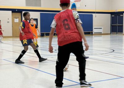 Two kids playing indoor soccer wearing red and yellow jerseys.