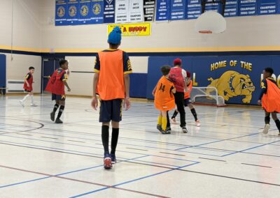 Youth playing indoor soccer in colorful jerseys and pinnies.