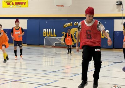 Adults and children playing indoor soccer in a gymnasium.
