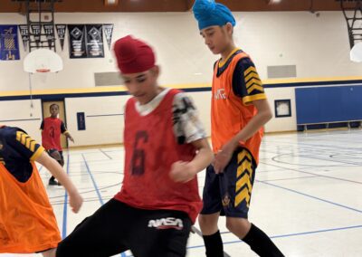 Two boys playing indoor soccer, one in red and one in orange.
