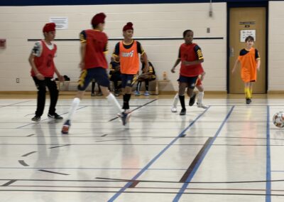 Children playing indoor soccer wearing red and orange jerseys.