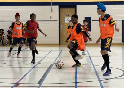 Children playing indoor soccer, wearing orange vests.