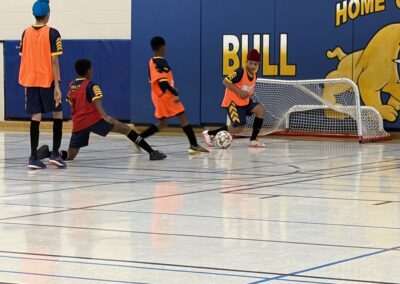Kids playing indoor soccer in a gymnasium.