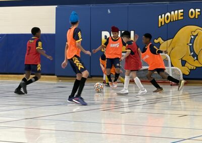 Kids playing indoor soccer wearing orange and red bibs.