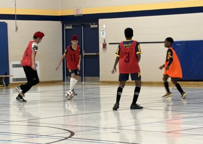 Young boys playing indoor soccer in a gymnasium.