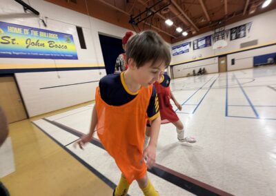 Two kids stretching in a gymnasium, one wearing an orange vest.