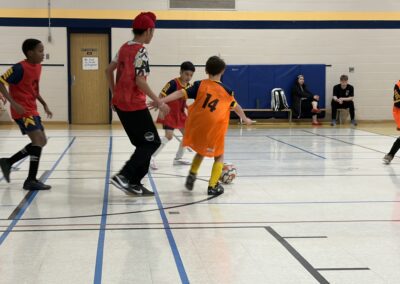 Youth basketball game with a player in a red jersey defending a young player in an orange jersey.