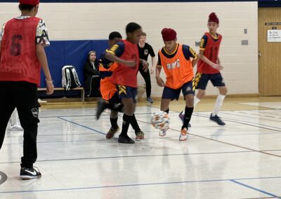 Young boys playing indoor soccer wearing orange and red jerseys.