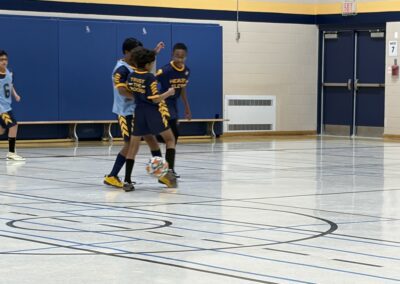 Two kids playing indoor soccer in blue and yellow uniforms.