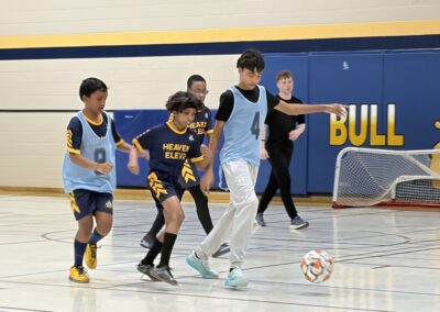 Kids playing an indoor soccer game in a gym.