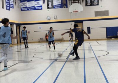 Boys playing basketball indoors in a school gymnasium.