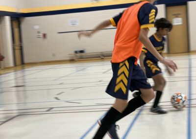 Two boys playing basketball indoors, one wearing an orange jersey.
