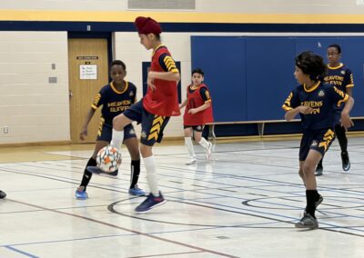 Boys playing indoor soccer, one in red controlling the ball.