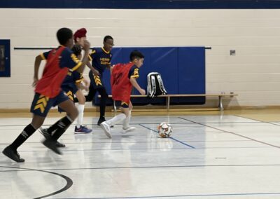 Young players sprinting to reach a soccer ball indoors.