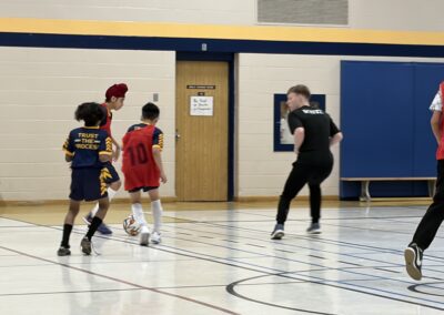 Kids playing indoor soccer while a coach watches closely.