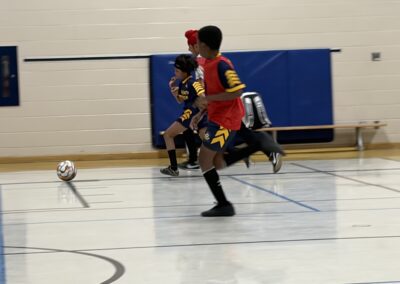 Two boys playing indoor soccer, chasing the ball.