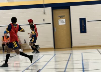 Two boys playing basketball indoors in colorful jerseys.