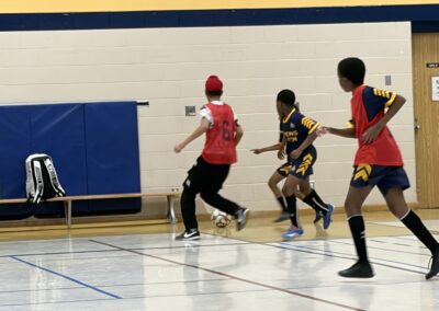 Indoor soccer game with players in action near the goal.