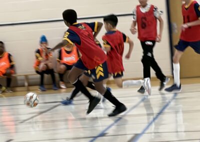 Children playing indoor soccer, chasing the ball intensely.