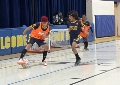 Two kids playing indoor soccer, one trying to steal the ball.