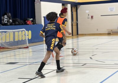 Two boys playing indoor soccer in a gymnasium.