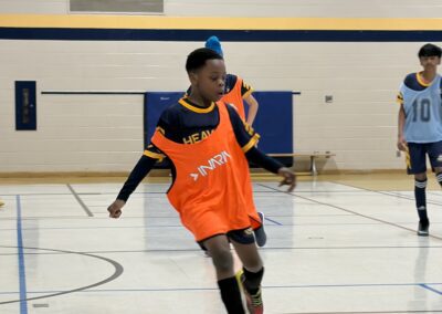 Young soccer player in an orange bib dribbling a ball indoors.