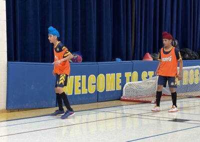 Two kids playing basketball indoors, wearing orange jerseys and headbands.