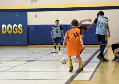 Young kids playing indoor soccer in a gymnasium.