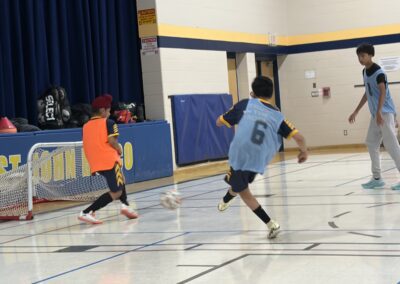 Two boys playing indoor soccer, one in an orange jersey and the other in a blue jersey.